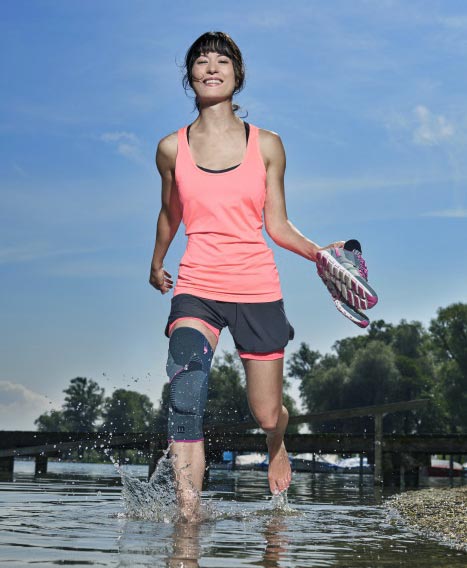 Frau mit Kniebandage geht barfuß durch Wasser