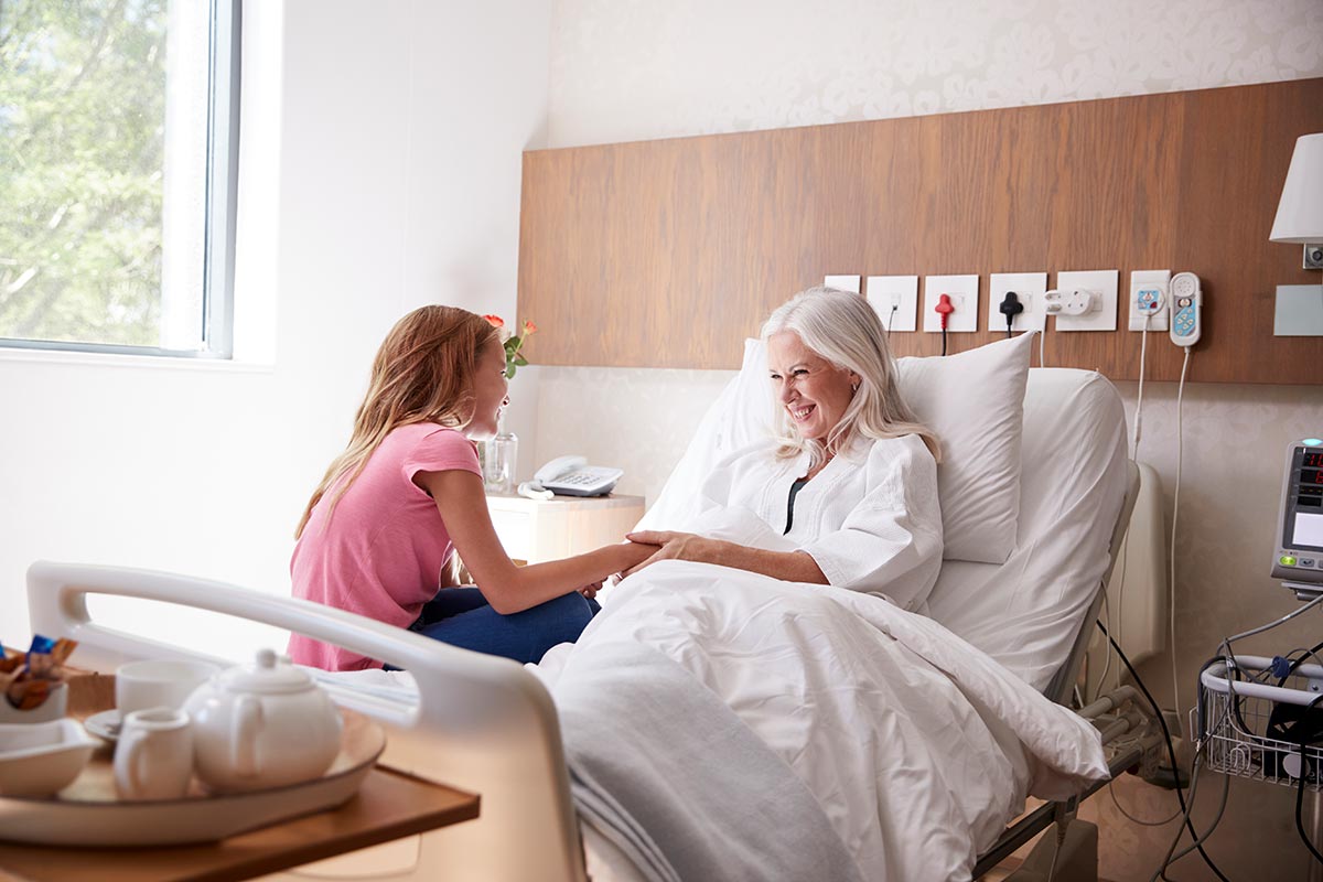 Ältere Frau liegt im Pflegebett und unterhält sich mit einem Kind